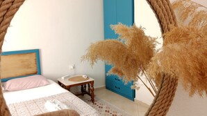 A round mirror with a rope frame reflecting a bedroom with a bed, a small table, a blue wardrobe, and dried plants. - Ayvalık Leya Pansiyon (Ayvalik)