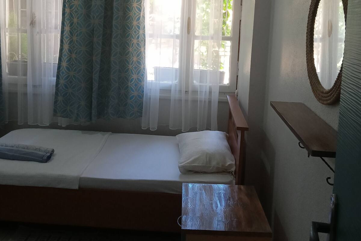 A single-bed room with a wooden headboard, a small bedside table, and a hanging rope decoration.