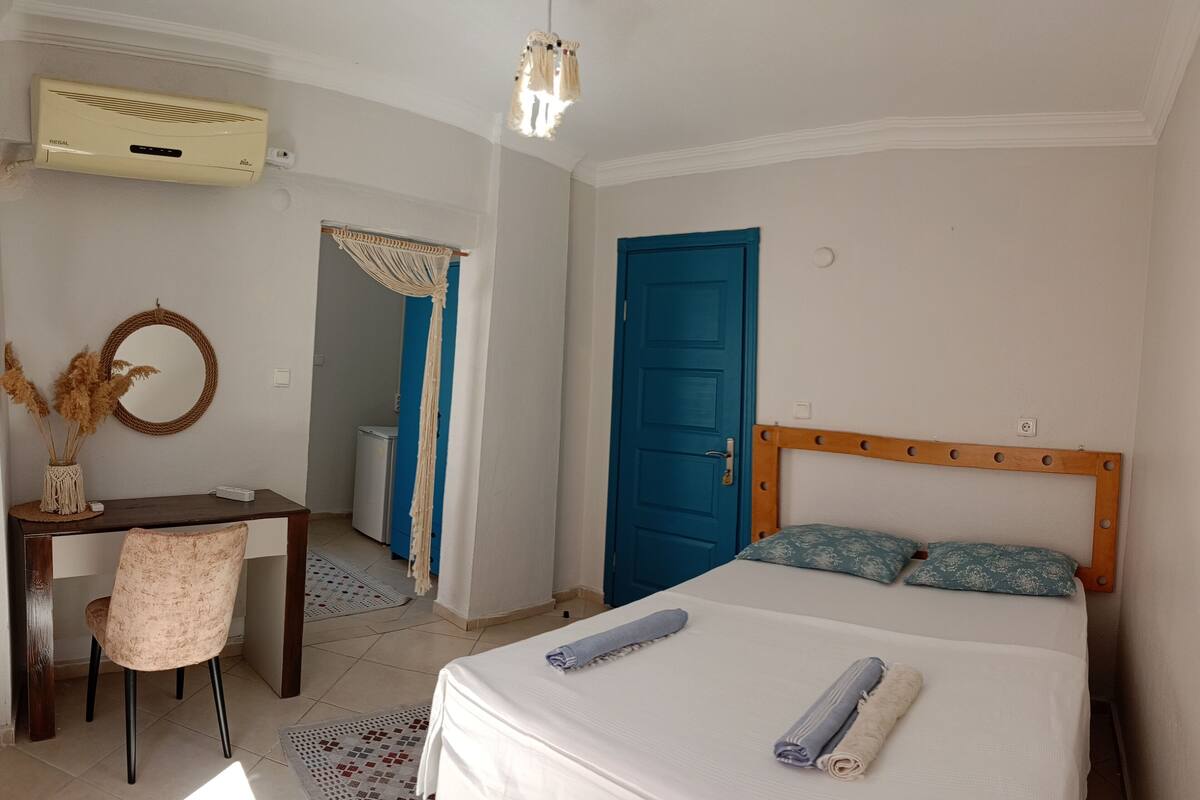 A bedroom with a bed, a desk, a chair, a wardrobe, and a bathroom visible through an open door.
