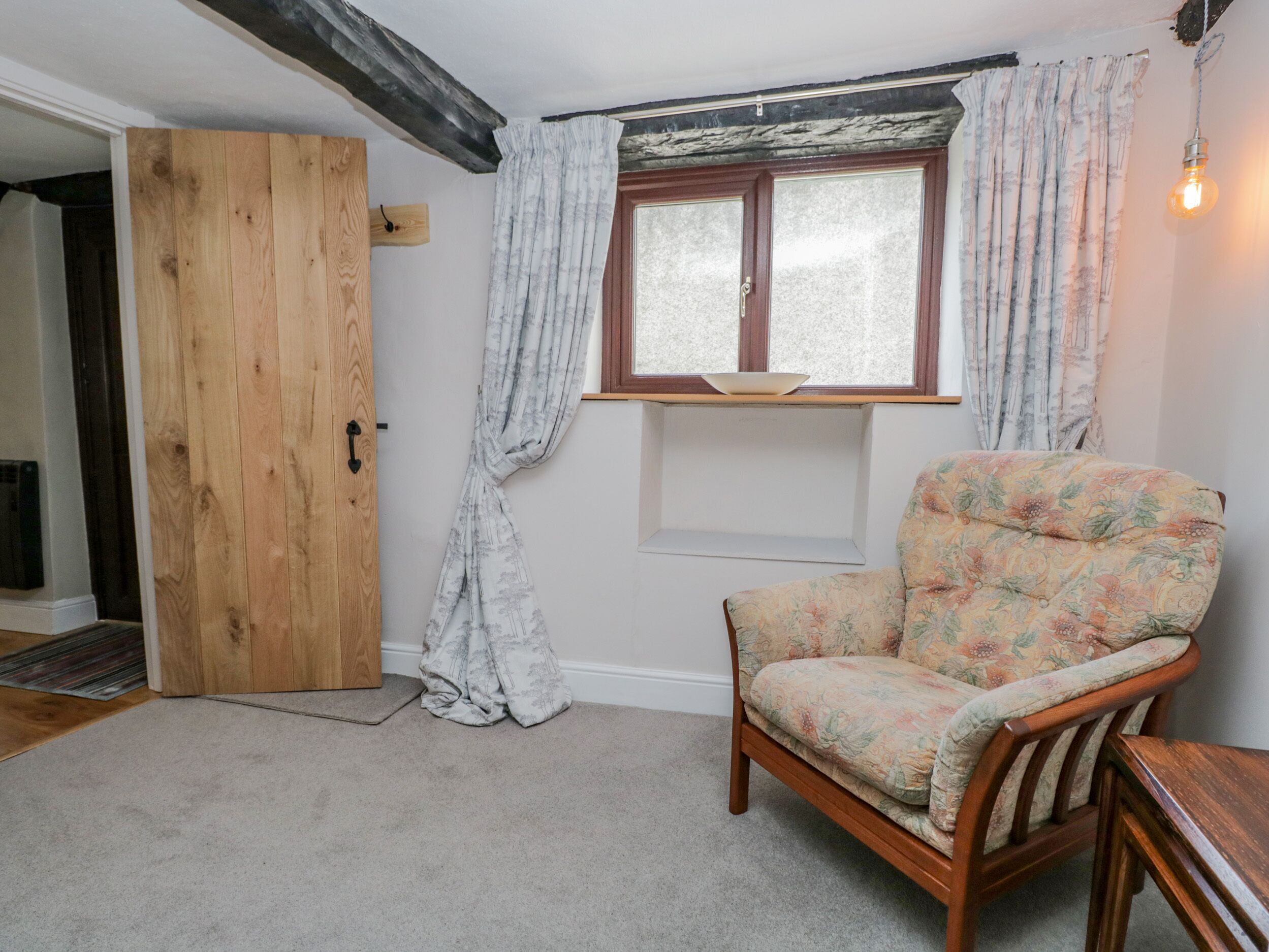 A room with a wooden door, a window with curtains, a floral armchair, and a light fixture.