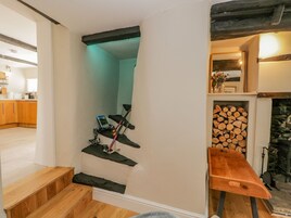 Una escalera con un banco de madera al final, una mesita con un florero y una pila de leña.