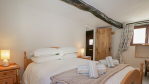 A neatly made bed with pillows and a blanket, wooden headboard, bedside tables with lamps, and a wooden door in the background. - Ashness (Keswick)