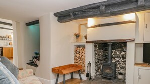 A cozy living room with a stone fireplace, wooden furniture, and a kitchen in the background. - Ashness (Keswick)