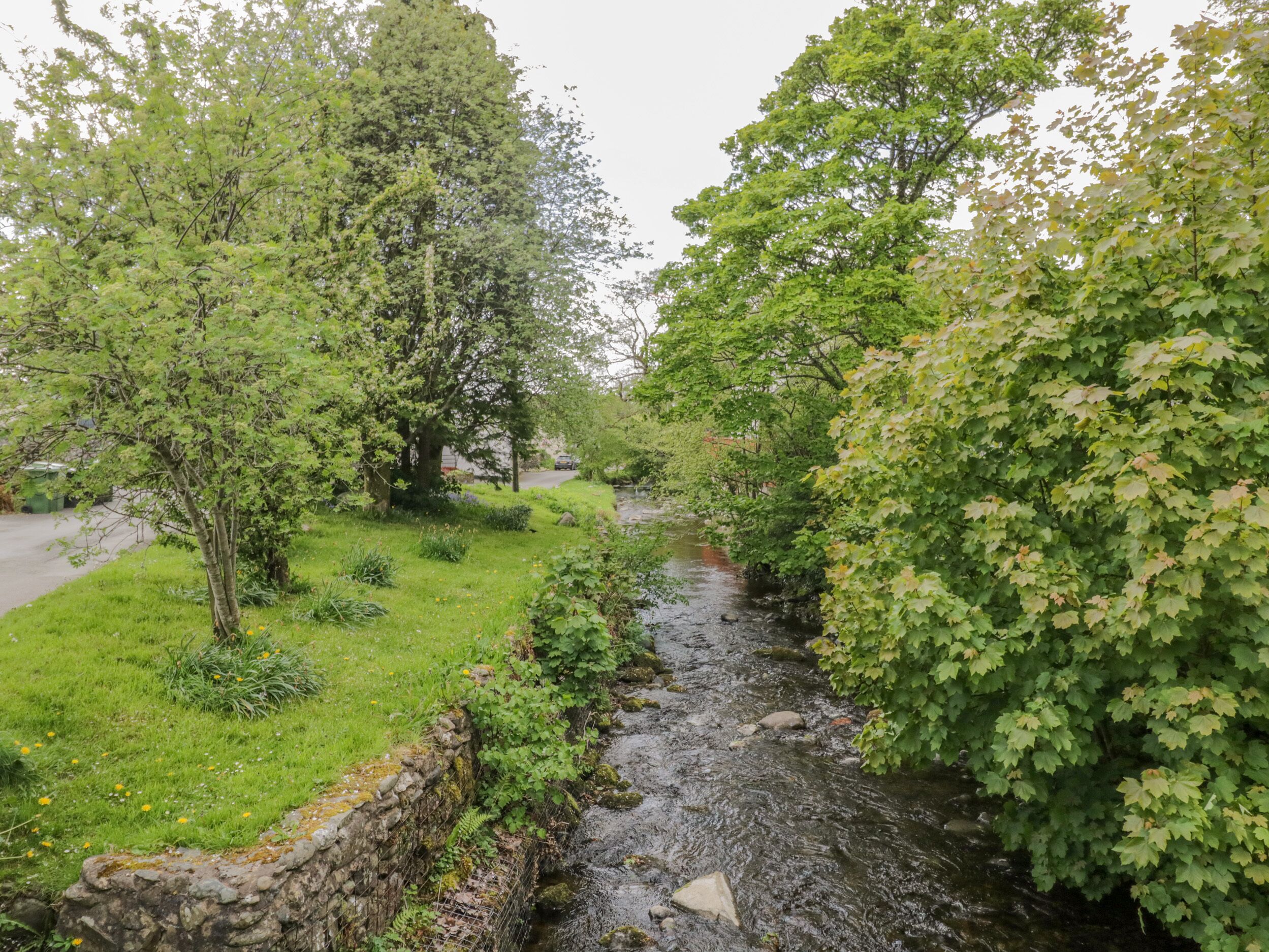 A stone wall alongside a stream in a park with trees and grass.