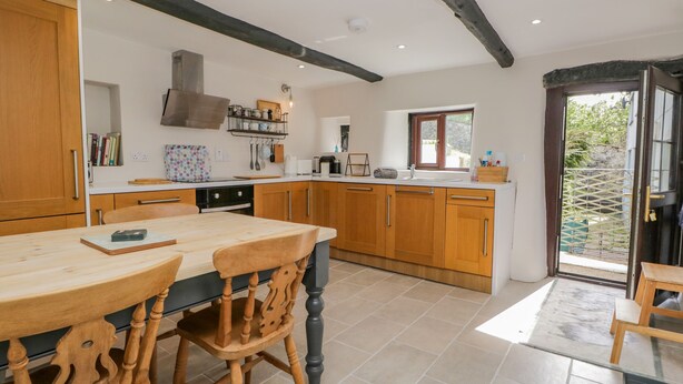 A modern kitchen with wooden cabinets, a dining table, and chairs. There is a window providing natural light and a view of the outdoors. - Ashness (Keswick)