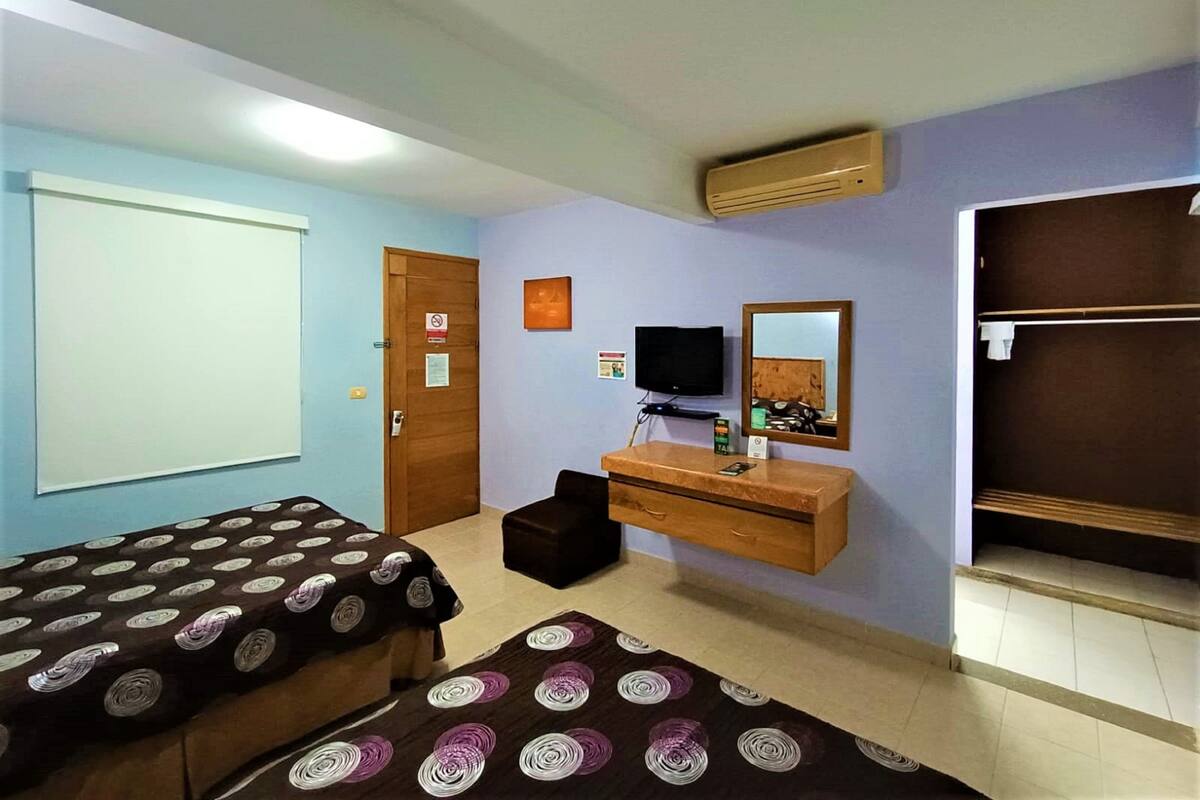 Habitación de hotel con dos camas, televisión, cómoda de madera y espejo.