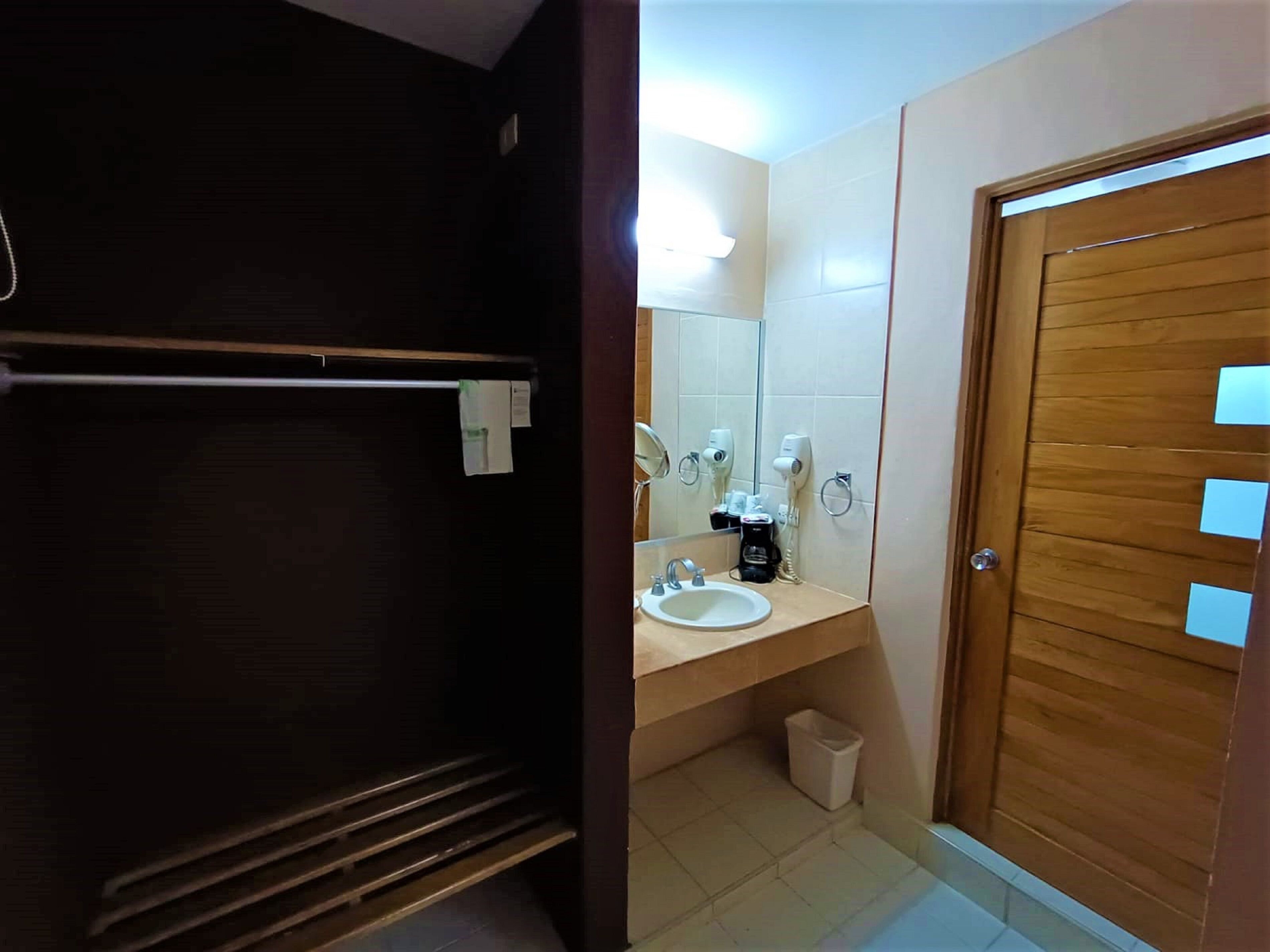 A bathroom with a wooden door, a sink, a mirror, a towel rack, and a trash bin.