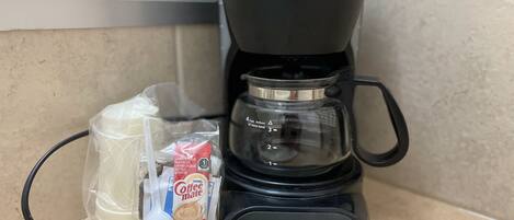 Máquina de café Mr. Coffee com jarra de vidro e um pacote de Creme de Café Nestle em uma bancada de cozinha.