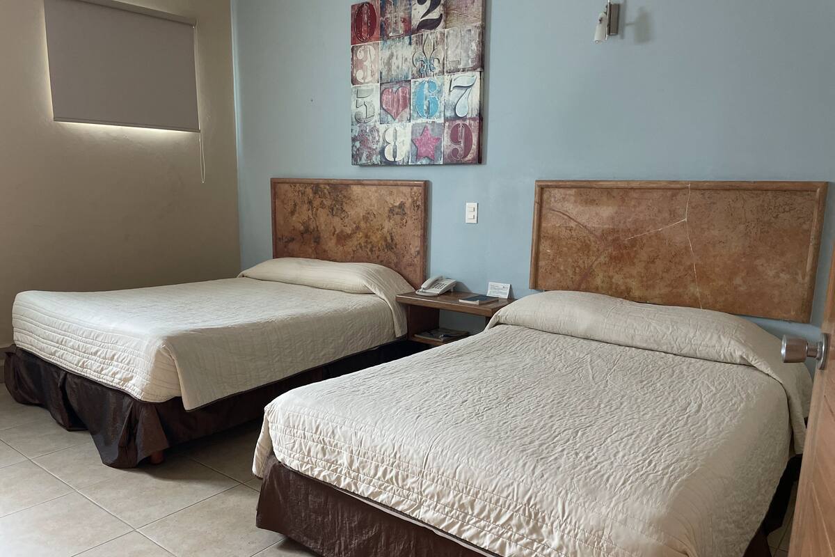 Una habitación de hotel con dos camas, una mesita de noche, un teléfono y una obra de arte en la pared.