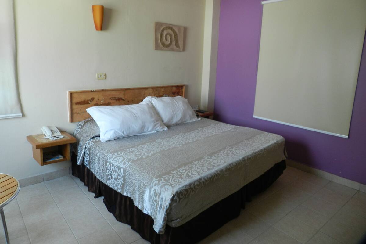 Un dormitorio con cama, mesita de noche, teléfono y lámpara de pared.