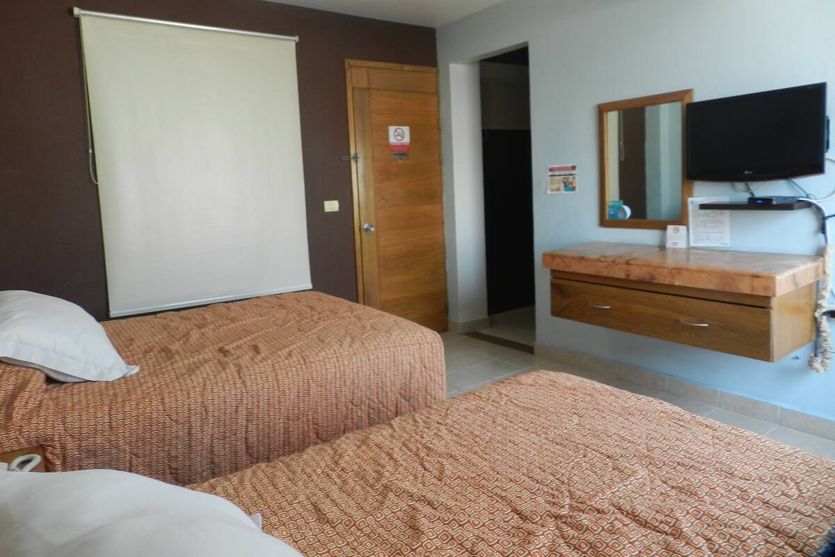 Una habitación de hotel con dos camas, un aparador de madera, un televisor y una puerta con un letrero.