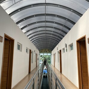 Een gang met een gebogen metalen plafond, houten deuren en een centrale trap.