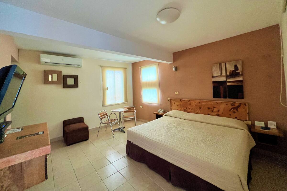 Habitación de hotel con cama, escritorio, silla, televisor y aire acondicionado.