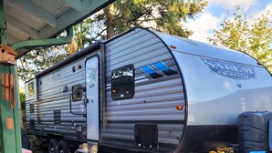 A large RV parked in a gravel area with a covered porch and a small table with flowers. - RV Glamping in the Heart of Downtown Eatonville with a Mountain View (Eatonville)