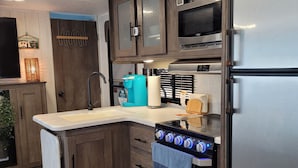 A compact kitchen with a built-in oven, a coffee maker, and a refrigerator. - RV Glamping in the Heart of Downtown Eatonville with a Mountain View (Eatonville)