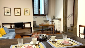 Un coin repas avec une table en bois dressée pour deux personnes, un canapé, un téléviseur et des tableaux encadrés accrochés au mur.
