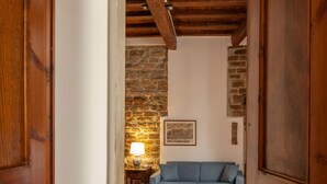 Une porte en bois donne sur une pièce où se trouvent un canapé bleu, une lampe et un mur en pierre.