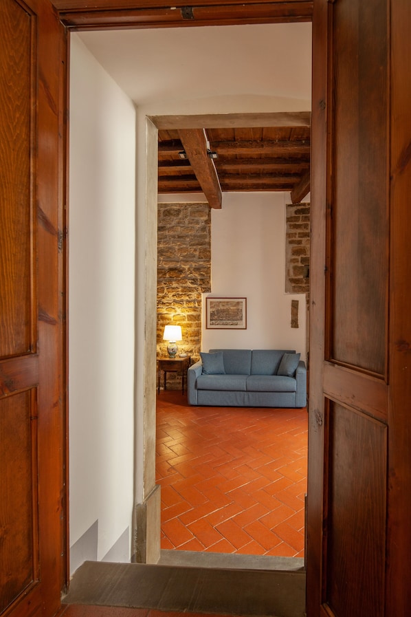 A wooden door leading into a room with a blue sofa, a lamp, and a stone wall.