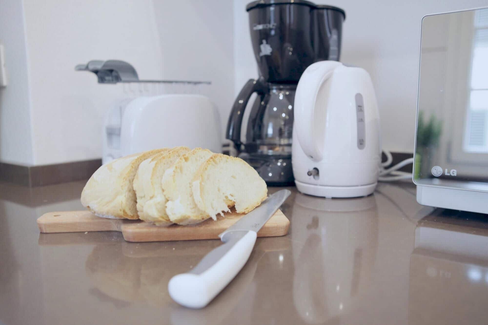 Un plan de travail de cuisine avec une miche de pain, un couteau, une machine à café et un mixeur.