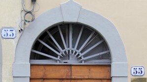 A double wooden door with a metal arch above it, flanked by two numbered signs, one above and one below the door. - Santa Reparata in Firenze (Florence)