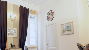 A living room with a brown sofa, a chair, a table, a clock, and a window with curtains. - Santa Reparata in Firenze (Florence)