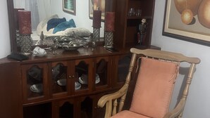 Un saló amb un moble de fusta, una cadira amb coixí i un gran mirall que reflecteix l'espai.