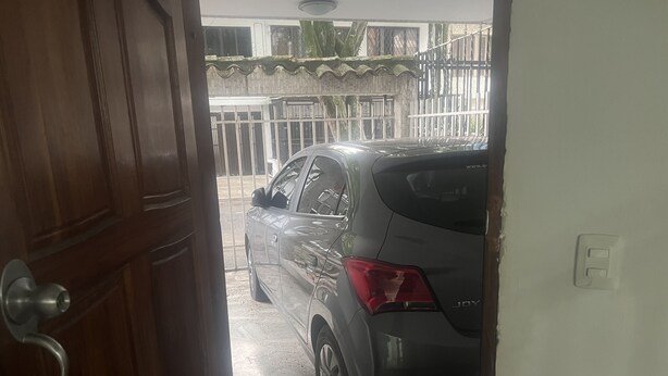 Un cotxe estacionat a la entrada d'una casa, amb una porta de fusta i una reixa metàl·lica al fons.