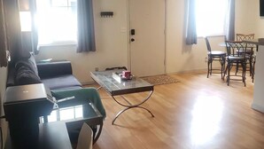 Una sala de estar con sofá, una mesa de centro de vidrio y un comedor con mesa y sillas.