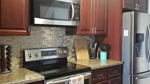 Una cocina con microondas, estufa y refrigerador de acero inoxidable, armarios de madera y salpicadero de azulejos.