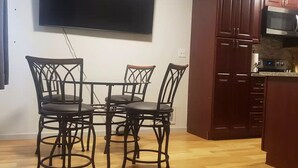 Un comedor con una mesa y cuatro sillas, un televisor de pantalla plana montado en la pared y armarios de madera en la cocina.