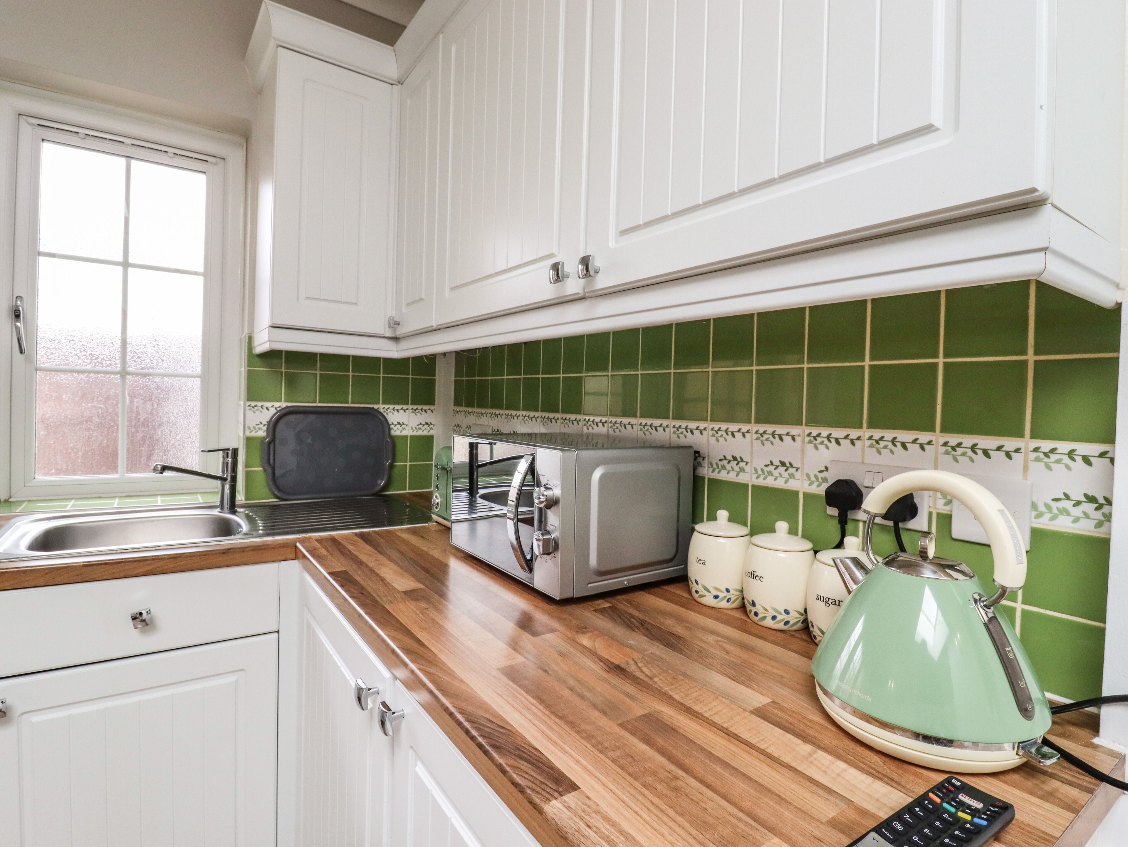 A kitchen with white cabinets, a green tiled backsplash, a toaster, a kettle, and a coffee maker.