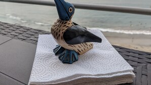Une statuette d’oiseau, posée sur une surface texturée près d’une rambarde donnant sur l’océan.