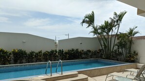 Une piscine avec un jacuzzi, entourée de palmiers et dotée d’une terrasse carrelée avec des chaises longues.