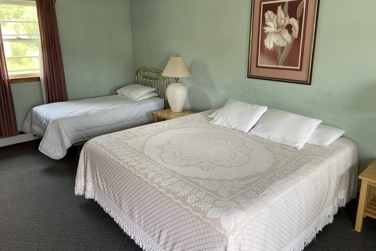 Une chambre avec deux lits simples, une table de chevet avec une lampe et une œuvre d’art florale encadrée au mur.