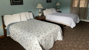 Een hotelkamer met twee bedden, een nachtkastje met lampen, en ingelijste foto's aan de muur.