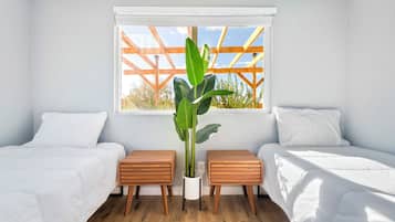 Een slaapkamer met twee bedden, een raam met houten kader en een kamerplant.