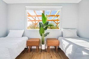 A bedroom with two beds, a window with a wooden frame, and a potted plant.