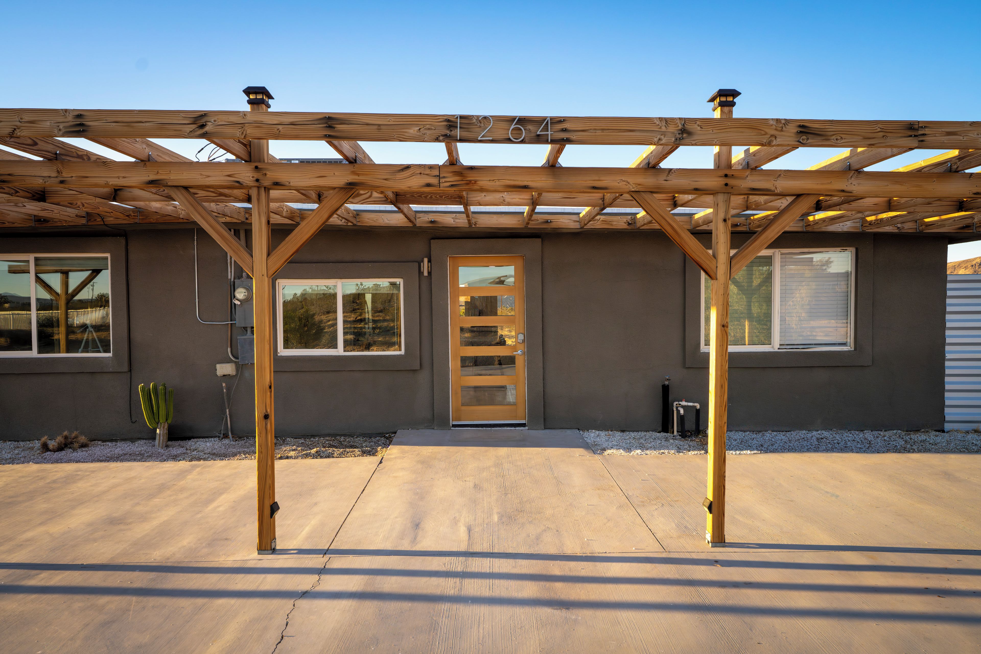 A building with a wooden pergola structure, a front door, and multiple windows.