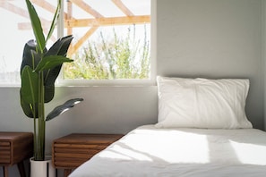 A bedroom with a bed, a window, a plant, and wooden nightstands. - Desert Oasis: Firepit, Stars, 5 Acres, Joshua Trees (Landers)