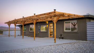 A modern house with a wooden pergola structure, large windows, and a gravel driveway.