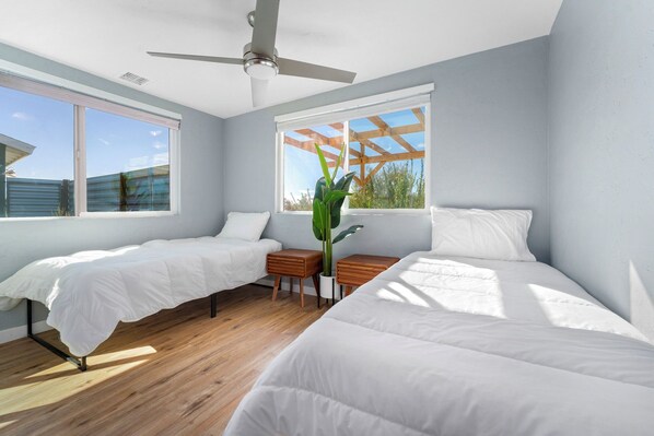 A bedroom with two beds, a ceiling fan, and a window with a wooden frame.