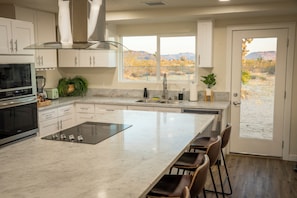 A modern kitchen with a large island, built-in appliances, and a view of a desert landscape. - Desert Oasis: Firepit, Stars, 5 Acres, Joshua Trees (Landers)
