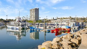 Un port esportiu amb vaixells, un edifici alt i una costa rocosa.