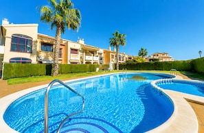 Une piscine à l’eau d’un bleu cristallin, entourée de palmiers et bordée d’un bâtiment doté de balcons.