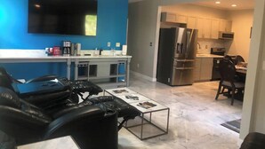 Una sala de estar moderna con un sofá de cuero negro, una mesa de centro y un televisor de pantalla plana montado en una pared azul.