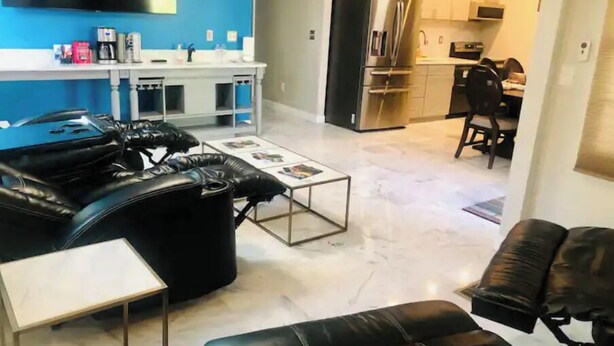 Una sala de estar moderna con un sofá de cuero negro, una mesita de centro y un televisor montado sobre una pared azul.