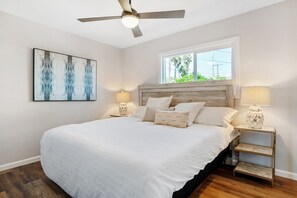 A bedroom with a bed, a ceiling fan, a window, and a wall-mounted artwork.