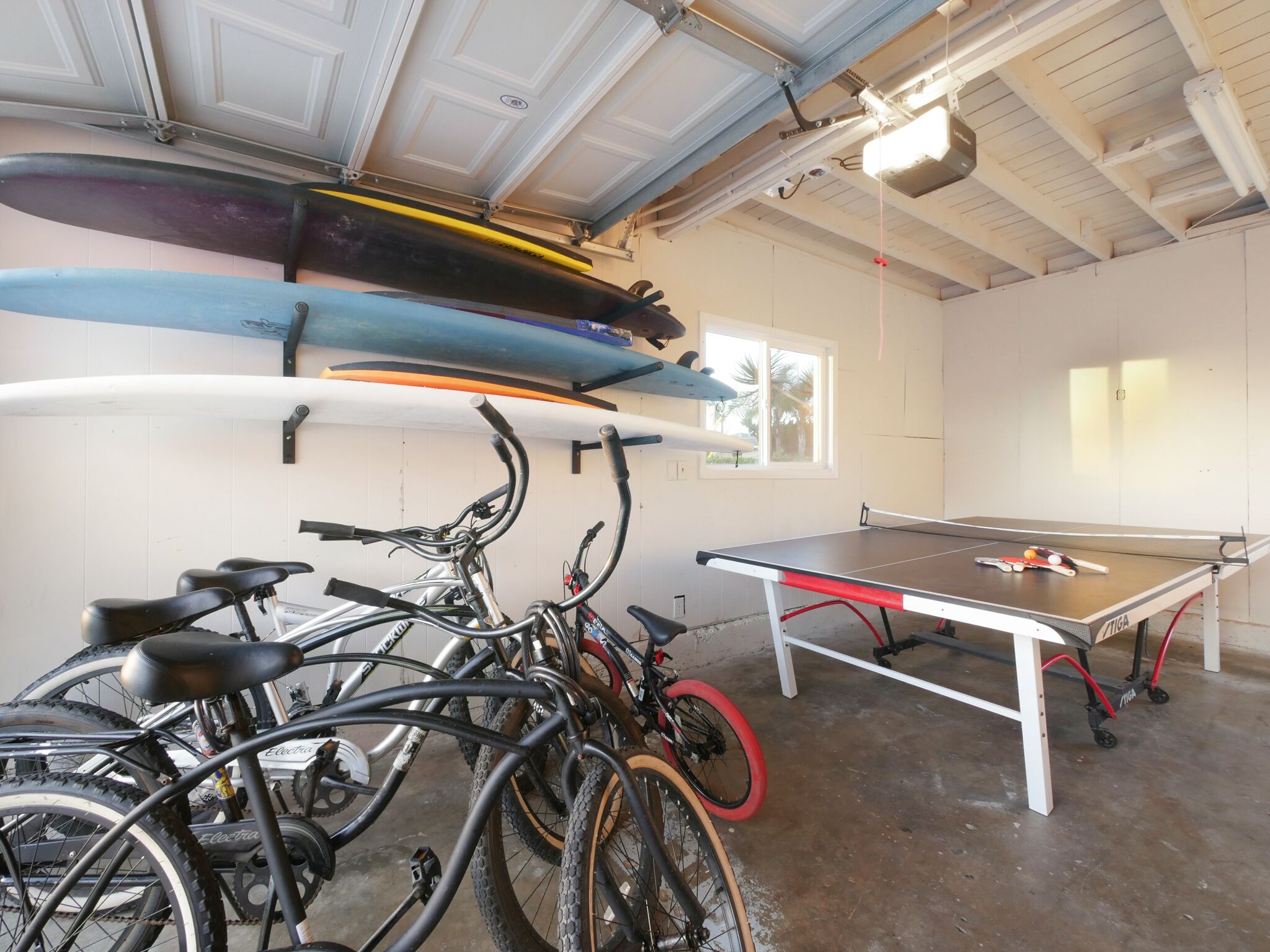 A room with bicycles, a ping pong table, and surfboards on a wall.