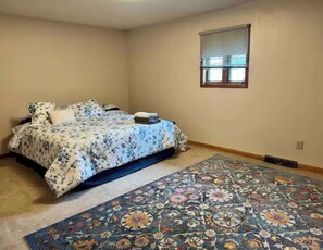 A bedroom with a bed, a window, and a patterned rug.