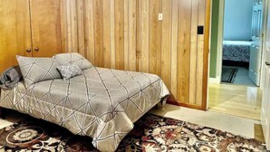 A bedroom with a bed, wooden walls, a patterned rug, and a door leading to another room. - Spacious 4 bedroom- Great Location (Lexington)